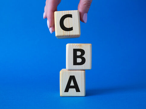CBA - Cost Benefit Analysis symbol. Wooden cubes with word CBA. Beautiful blue background. Businessman hand. Business and Cost Benefit Analysis concept. Copy space.