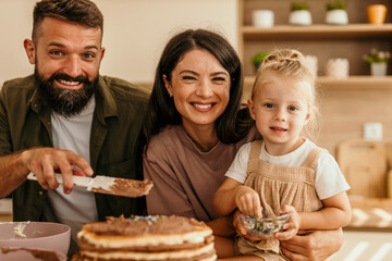 Family decorating homemade cake in kitchen smiling