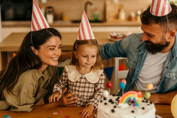 Family celebrating a child's birthday with a cake and party hats