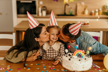 Loving parental couple giving child kisses celebrating birthday