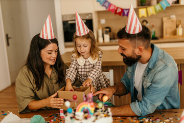 Little girl opening birthday present with parents