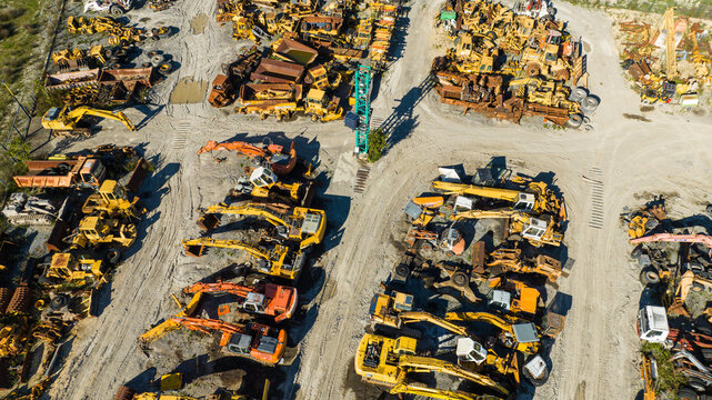 Aerial view of a sprawling junkyard filled with rusting yellow and orange heavy machinery contrasting against the stark, grey earth, Nanclares de la Oca, Basque Country, Spain.