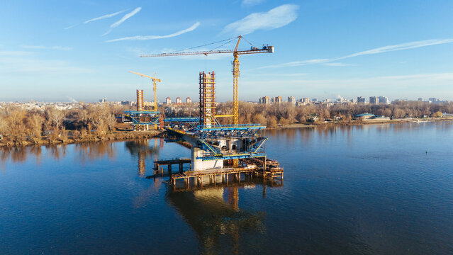 Aerial view of the Zezelj Bridge under construction reflecting in the river contrasting with the cityscape, Novi Sad, Vojvodina, Serbia.