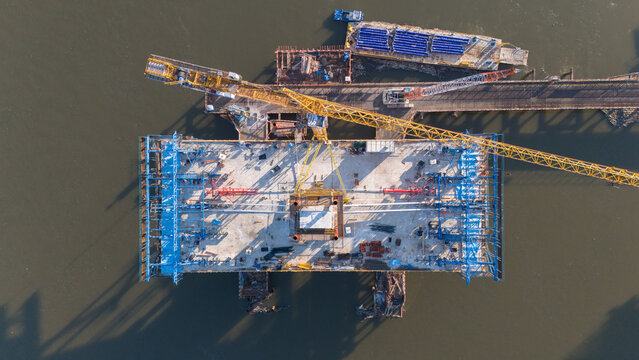 Aerial view of a massive bridge section under construction with cranes and equipment casting long shadows on the water, Novi Sad, Vojvodina, Serbia.