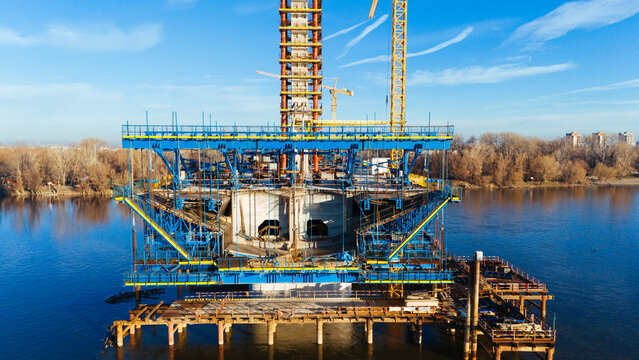 Aerial view of a bridge under construction with blue steel framework rising from the water against the backdrop of the city, Novi Sad, Vojvodina, Serbia.
