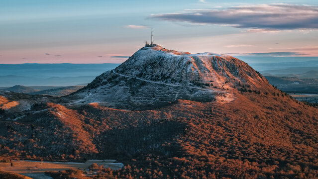 Aerial view of the majestic Puy de Dome, capped with snow, stands sentinel beneath a pastel sky, a beacon amidst the undulating landscape, Orcines, Auvergne-Rhone-Alpes, France.