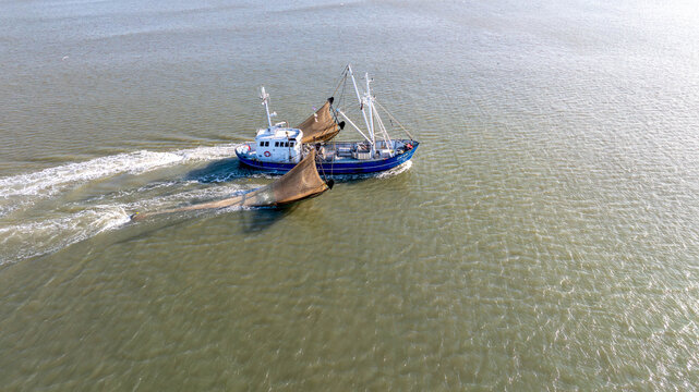 Aerial view of a fishing boat sailing through the calm, shimmering waters, leaving a foamy trail in its wake, Wijk aan Zee, North Holland, Netherlands.