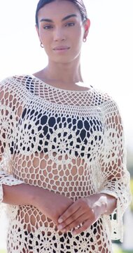 Vertical video: Woman modeling outdoors clasping hands, camera rising, smiling in crochet coverup