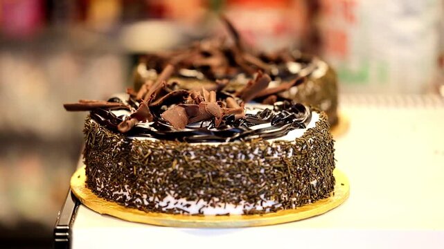 Slow Motion Shot of Chocolate cake adorned with sprinkles and chocolate shavings displayed on a bakery counter with soft lighting at 180 fps High quality footage