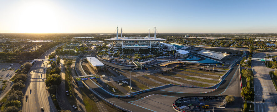 Miami Gardens, Florida - 23 February 2026: Aerial view of Hard Rock Stadium bathed in the golden light of the setting sun, surrounded by the winding race track and lush greenery.