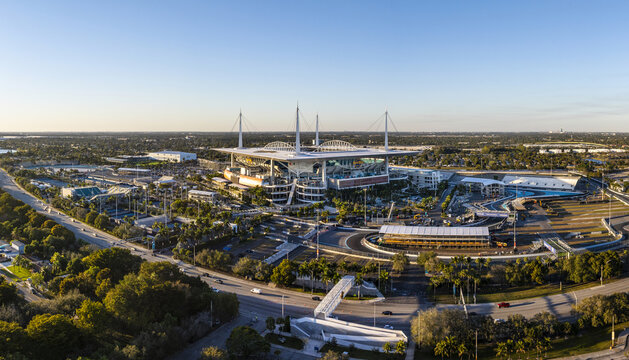 Miami Gardens, USA - 23 February 2026: Aerial view of Hard Rock Stadium, a modern coliseum bathed in the warm glow of the setting sun, surrounded by verdant trees and bustling roadways.
