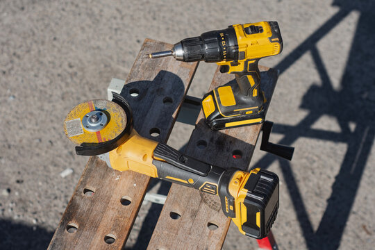 Yellow cordless drill, battery powered impact driver, and angle grinder with cutting disc arranged on a workbench. Concept for construction power tools, DIY repair equipment and handyman tools.
