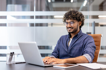 Smiling Indian man working in the office at a laptop