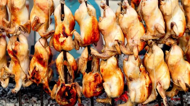 Slow Motion Shot of Roasted chickens hanging and being cooked over charcoal grill with visible smoke and intense heat creating a barbeque event at 180 fps High quality footage