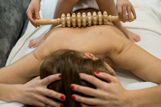 A tender moment of family wellness where a young child uses a wooden maderotherapy tool to give a gentle back massage to a woman