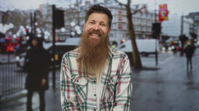 Man with shaggy beard clad in green plaid shirt glances sideways on busy street in cityscape; contentment.
