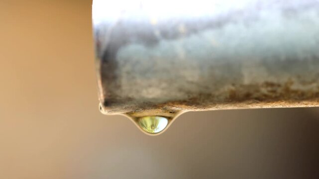 Slow Motion Shot of Water drop hanging from a weathered metal pipe in warm, ambient lighting showing surface tension and the effects of rust at 180 fps High quality footage