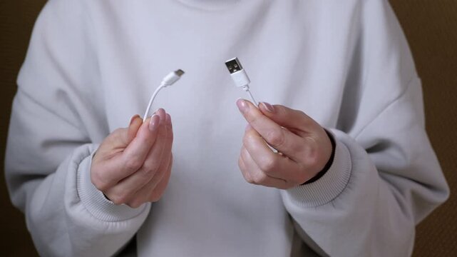 Woman holding broken usb type-c cable. Woman's hands holding the two ends of a broken or cut white usb charging cable, demonstrating the concept of damaged technology, connectivity issues