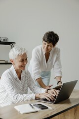 Fototapeta premium Two mature women working together on laptop at wooden desk