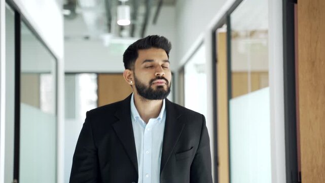 Businessman in formal suit walks along corridor of office building during working day. Confident male manager going to a meeting through modern bright hall of business center, looking away.