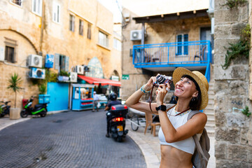 Cheerful smiling woman walking along the street of the old city in an Arab country and taking pictures of sights for social networks. Girl with a phone.
