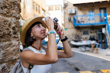 Cheerful smiling woman walking along the street of the old city in the Arab country. Stylish traveler taking pictures of sights for social networks.