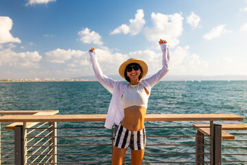 The girl enjoys her vacation. A slender woman stands on the embankment near the sea and enjoys the moment. Summer vacation by the sea.