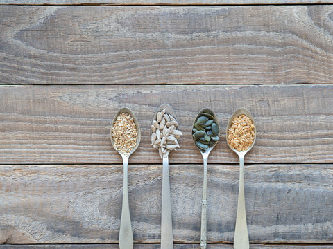 Healthy seeds in spoons on wooden background