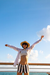 Slender woman stands on the embankment and looks at the ocean. Summer vacation by the sea. Freedom and relaxation on the seashore.