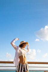 Slender woman stands on the embankment and looks at the ocean. Summer vacation by the sea. Freedom and relaxation on the seashore.