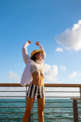 Slender woman stands on the embankment and looks at the ocean. Summer vacation by the sea. Freedom and relaxation on the seashore.
