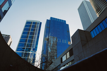 Obraz premium Tall buildings rise against a clear sky in a busy city during daytime with sunlight reflecting off glass windows and structures