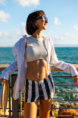 Girl enjoying her vacation. Slender and attractive woman standing on the embankment by the sea and enjoying the moment. Smiling brunette. Confident girl standing by the sea.