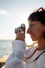 Girl taking pictures. Beautiful tourist enjoying sea view during weekend vacation and taking a picture with film camera. Girl with camera.