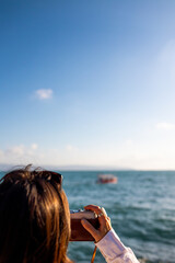 girl taking picture of ship standing on embankment. Beautiful female tourist enjoying sea view while relaxing on weekend. girl using camera.