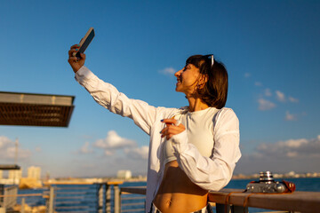 Female blogger shoots content for social networks. Smiling tourist takes a selfie on her mobile phone against the backdrop of the sea.