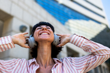 A happy white woman, relaxed and carefree, walks down the street, listening to music on headphones and dancing to the beat. Listening to her favorite song.