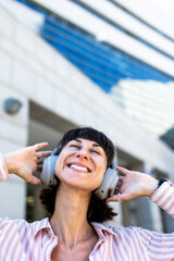 A happy white woman, relaxed and carefree, walks down the street, listening to music on headphones and dancing to the beat. Listening to her favorite song.