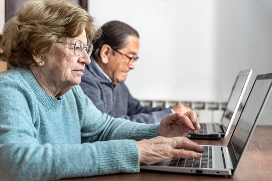 Active senior adults learning digital skills on laptops in classroom.