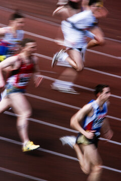 Abstract panning shot of sprinters racing on a track during competition. Vintage 35mm film scan, motion blur. Acceleration, speed, intense rhythm of athletics performance in stadium setting.