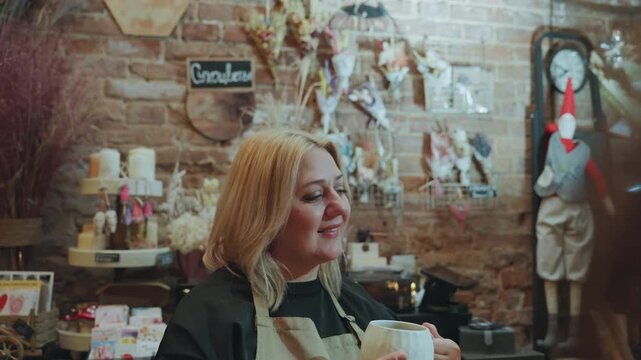 Blonde florist chatting behind shop counter, woman in apron smiling among dried bouquets and quirky decor, brick wall display with gifts and tags, warm inviting energy and friendly service vibe