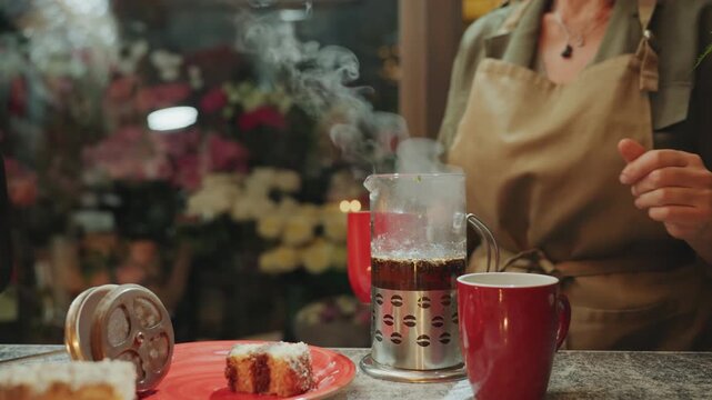 Customer enjoying warm beverage among colorful flowers. Serene setting with smiling customer sipping tea amid bright blooms. Charming floral shop scene showing customer with red mug and gentle smile