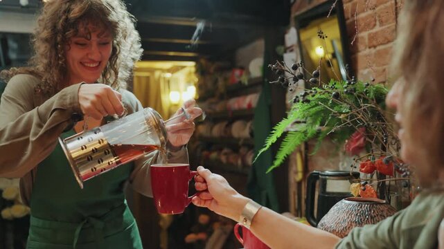 Customer enjoys warm tea amidst flowers. Gentle smile with aromatic tea in floral shop. Customer with tender smile savors steaming tea amidst blooming flowers and rustic brick decor