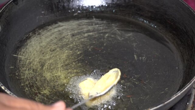 Dropping pakora batter into hot oil with a spoon