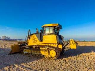 Obraz premium Heavy machinery works on a beach to prepare the sand for visitors on a clear sunny day near the ocean
