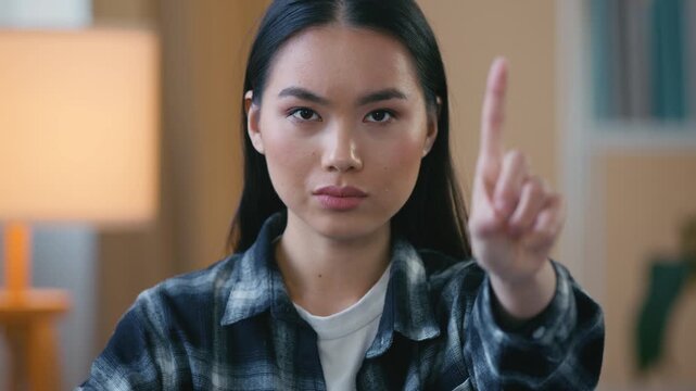 Serious Asian Korean woman at home holding index finger stop gesture Japanese female girl saying no reject dislike anti discrimination social issues domestic violence racism denial awareness indoors