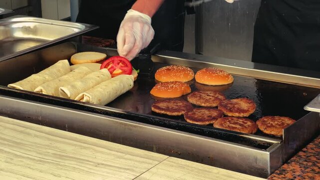 Cooking burger patties on a hot plate in an open kitchen. Fast food preparation, close-up.