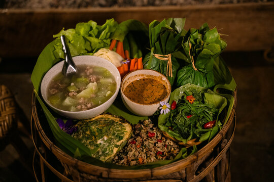 Traditional Akha tribal khantoke food set served in a bamboo tray with fresh vegetables, chili dip, soup and local northern Thai dishes. Authentic hill tribe cuisine from northern Thailand representin
