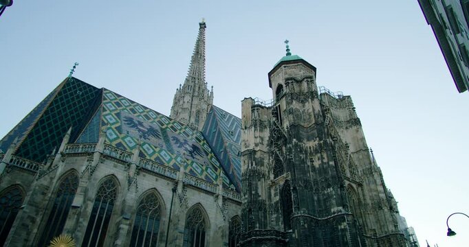 Cinematic wide low angle gimbal shot of St Stephens Cathedral in Vienna, Austria. Iconic colorful roof tiles and massive gothic spire against a clear summer sky. High-quality travel footage