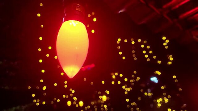 Close-up of a large, red C7 Christmas light bulb hanging in front of a bokeh background of smaller yellow lights.